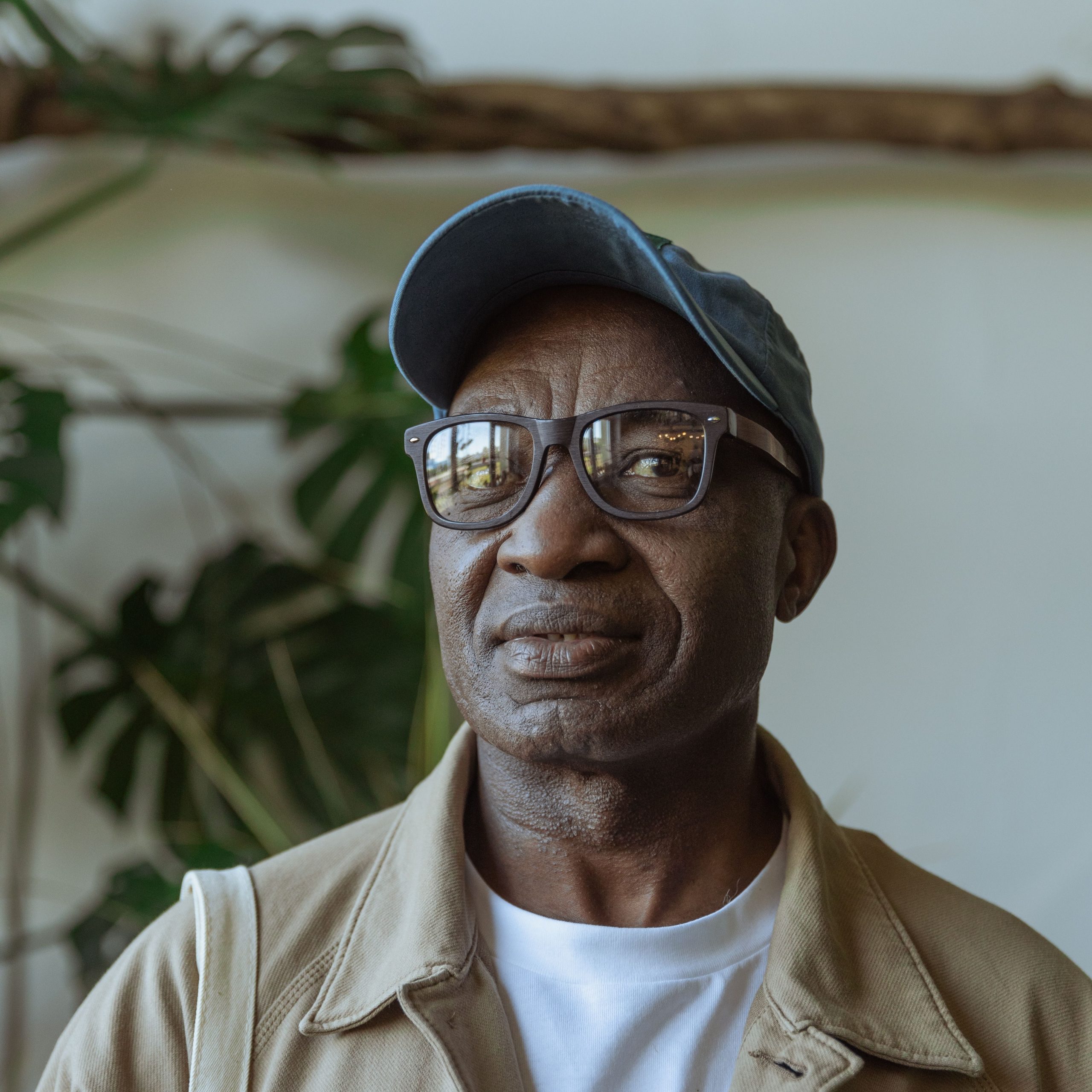testimonial-skip-02 Senior man smiling indoors wearing glasses and a baseball cap with indoor plants in the background.